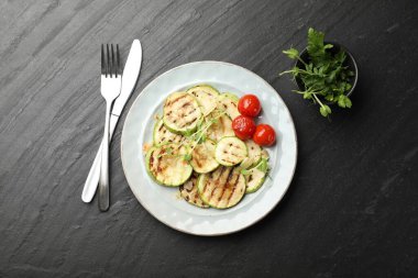 Lezzetli ızgara kabak dilimleri domatesli ve mikroyeşillikli siyah desenli masada servis ediliyor.