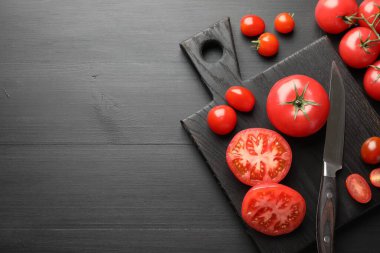 Siyah masanın üstünde bıçaklı kırmızı domatesler, düz bir şekilde. Metin için boşluk