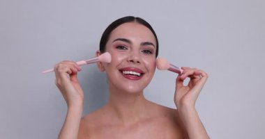 Açık gri arka planda makyaj fırçası olan güzel bir kadın.