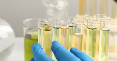 Bilim adamı deney tüplerindeki kirli suya beyaz masadaki büyüteçle bakıyor.