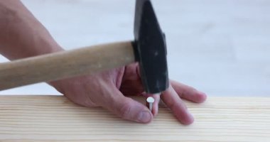 Kapalı alanda tahta çiviye çivi çakan bir adam var.
