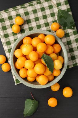 Olgun sarı kiraz erikleri, siyah ahşap masa üzerinde yapraklar, düz yatıyordu.