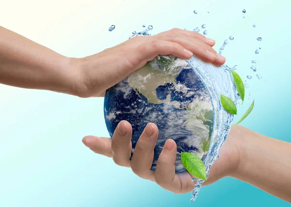 Su kavramını sakla. Dünya, mavi eğimli arka plana karşı insan ellerinde, yakın plan. Su sıçrıyor ve dünyanın her yerinde yeşil yapraklar
