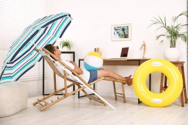 Güneş gözlüklü, plaj toplu bir adam kapalı bir masada güneşlenirken eğleniyor. Denizde tatilin hayalini kuruyorum.