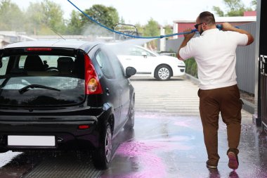 Adam oto yıkamada yüksek basınçlı su jetiyle araba yıkıyor.