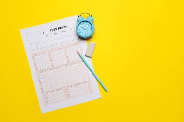 Öğrenci sınavını geçiyor. Cevap kâğıdı, alarm saati, sarı arka planda kalem ve silgi, düz konum. Metin için boşluk