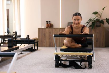 Pilates stüdyosunda reformist üzerinde egzersiz yapan bir kadın.