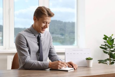 Ofisteki ahşap masada iş planlayıcısı kullanan adam.