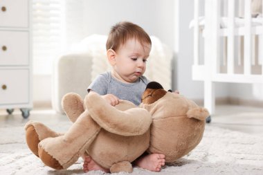 Küçük şirin bebek odada oyuncak ayıyla oynuyor.