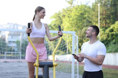 Dışarıda spor aletleriyle spor yapan genç bir kadın. Profesyonel spor hocasıyla.