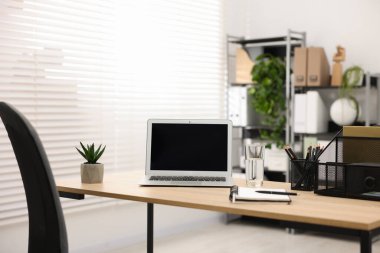 Ofisteki ahşap masada dizüstü bilgisayarı ve kırtasiyesi olan şık bir iş yeri.