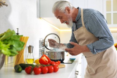 Mutfaktaki mutfağın tepesinde yaşlı bir adam yemek pişiriyor.