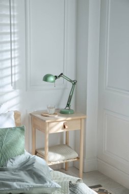 Yatak odasının yanında lamba ve bir bardak su olan komodinin yanında.