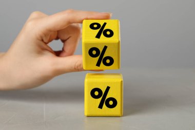 Gri arkaplanda yüzde işareti olan sarı küp tutan kadın, yakın plan.