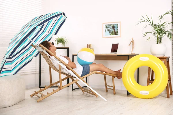 Güneş gözlüklü, plaj toplu bir adam kapalı bir masada güneşlenirken eğleniyor. Denizde tatilin hayalini kuruyorum.