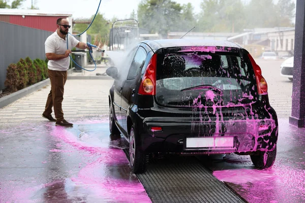 Adam oto yıkamada yüksek basınçlı su jetiyle araba yıkıyor.