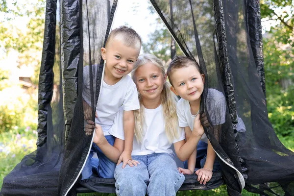 Dışarıda siyah trambolinde poz veren mutlu çocuklar.