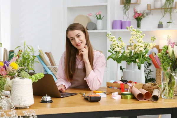 Dükkandaki tahta masada dizüstü bilgisayarla çalışan profesyonel bir çiçekçi.
