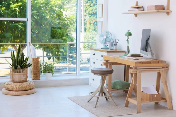 Ev çalışma alanı. Modern bilgisayar ve kırtasiye malzemeleri pencerenin yanındaki ahşap masada.
