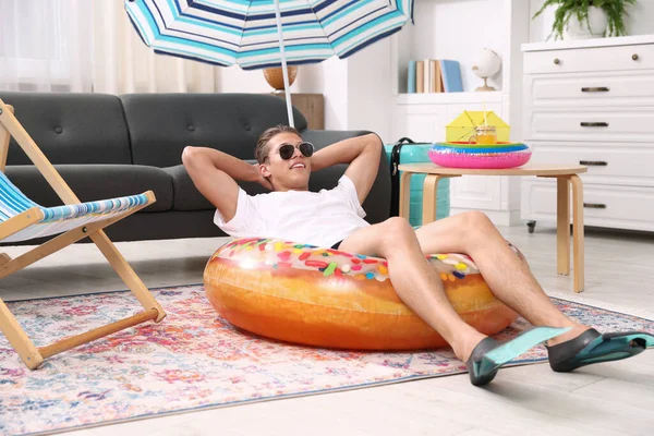Güneş gözlüklü mutlu adam ve şişme yüzüklü paletler evde yerde eğleniyor. Denizde tatilin hayalini kuruyorum.