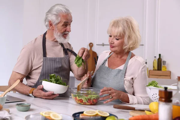 Yaşlı çift mutfaktaki masada birlikte yemek pişiriyor.