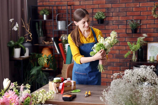 Profesyonel çiçekçi dükkandaki ahşap masada çiçek buketi yapıyor.