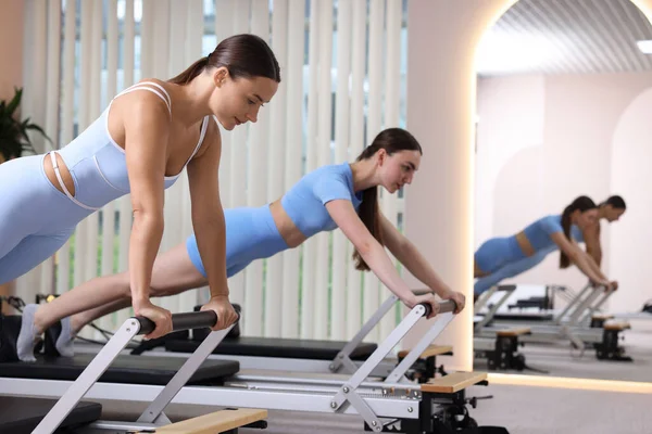 Stüdyoda reformcular üzerinde egzersiz yapan kadın ve pilates eğitmeni.