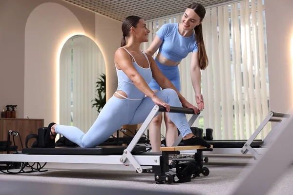 Stüdyoda pilates eğitmeni tarafından yönetilen reformcu kadın üzerinde egzersiz yapıyor.