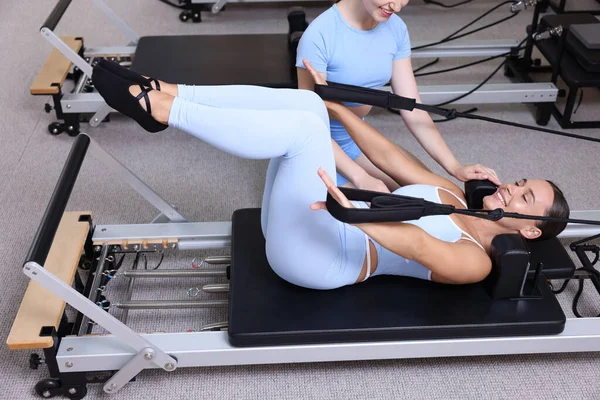 Stüdyoda pilates eğitmeni tarafından yönetilen reformcu kadın üzerinde egzersiz yapıyor.