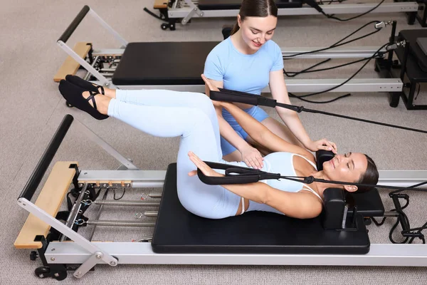 Stüdyoda pilates eğitmeni tarafından yönetilen reformcu kadın üzerinde egzersiz yapıyor.