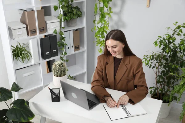 Ofiste dizüstü bilgisayarla çalışırken not alan bir kadın.