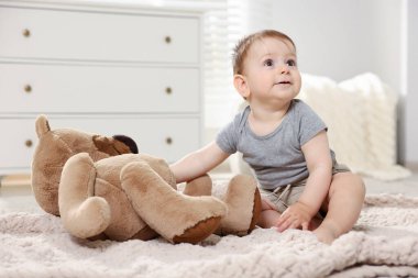 Küçük şirin bebek odada oyuncak ayıyla oynuyor.