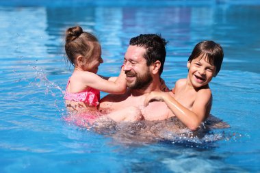 Mutlu baba ve çocukları açık havuzda dinleniyorlar. Aile tatili