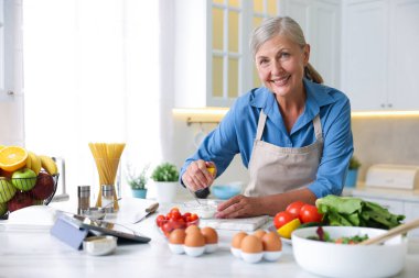 Üst düzey kadın mutfaktaki beyaz mermer masada yemek pişiriyor.