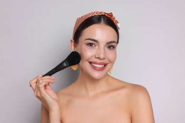 Açık gri arka planda fırçayla makyaj yapan güzel bir kadın.