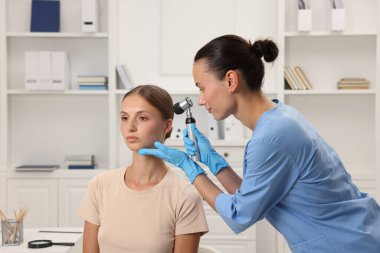 Doktor hastanede dermatoskopla genç kadının benini inceliyor.