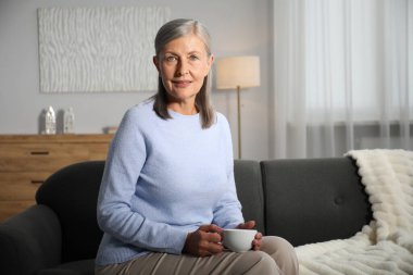 Evdeki kanepede çay içen yaşlı kadın.