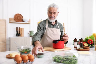 Mutfaktaki beyaz mermer masada yaşlı bir adam yemek pişiriyor.