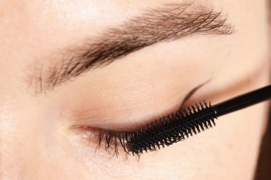 Bir kadın kirpiklerine rimel sürüyor, yakın plan.