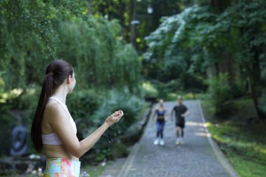 Genç adam ve kadın profesyonel antrenörle dışarıda egzersiz yapıyor, seçici bir odak noktası var.