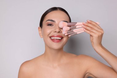 Açık gri arka planda makyaj fırçası olan güzel bir kadın.