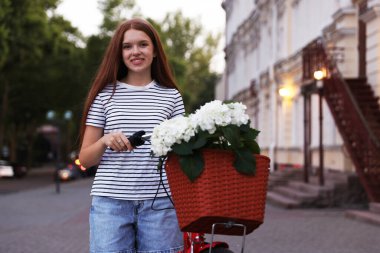 Bisikletin yanında güzel bir genç kız ve şehir caddesinde bir sepet çiçek.