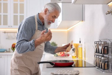 Mutfaktaki mutfağın tepesinde yaşlı bir adam yemek pişiriyor.