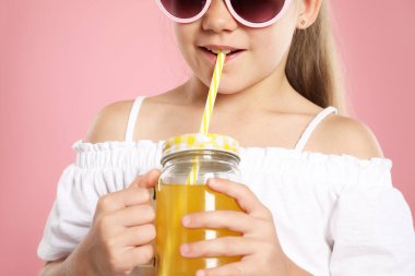 Küçük kız pembe arka planda samandan meyve suyu içiyor, yakın plan.