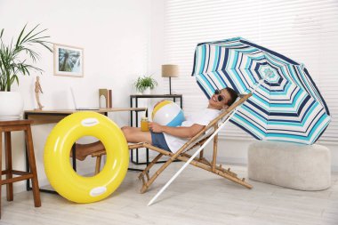 Güneş gözlüklü mutlu bir adam. Kavanoz dolusu meyve suyu ve plaj topu ile evde güneşlenirken eğleniyor. Denizde tatilin hayalini kuruyorum.