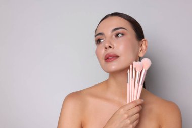 Açık gri arkaplanda makyaj fırçaları olan güzel bir kadın, metin için boşluk