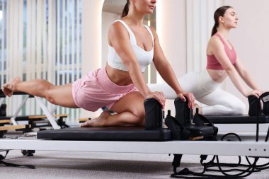 Stüdyoda reformcular üzerinde egzersiz yapan kadın ve pilates eğitmeni.
