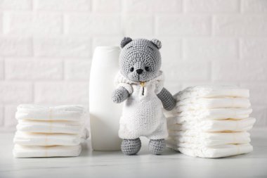 Bebek bezleri, şampuan ve oyuncak ayı tuğla duvarın yanındaki beyaz masada.