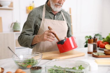 Mutfaktaki beyaz mermer masada yaşlı bir adam yemek pişiriyor.
