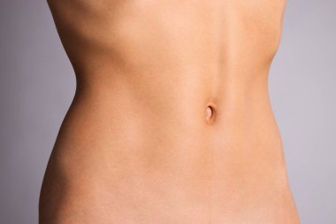 Gri arka planda düz göbekli kadın, yakın plan.